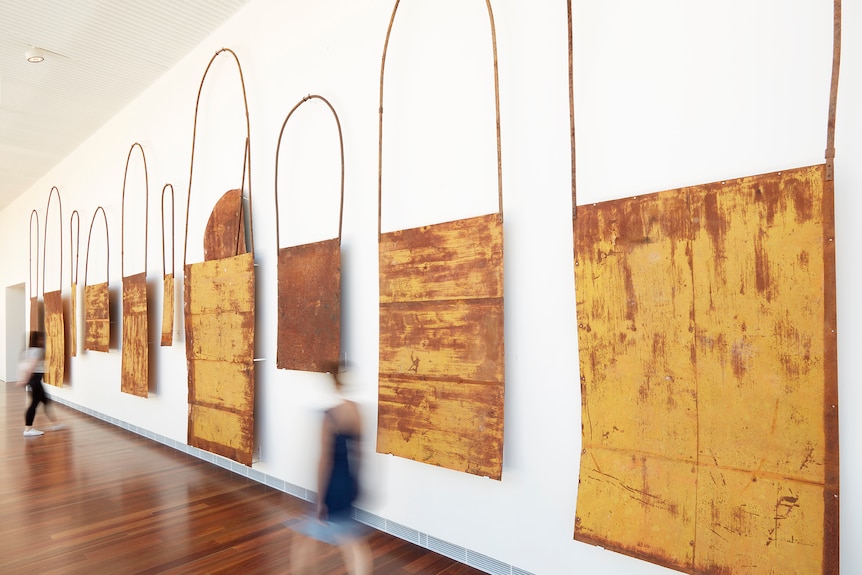 A series of large orange bags hanging on a white gallery wall