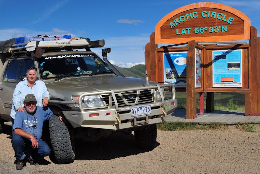 A man and a woman with their four-wheel drive near a sign that says Arctic Circle.