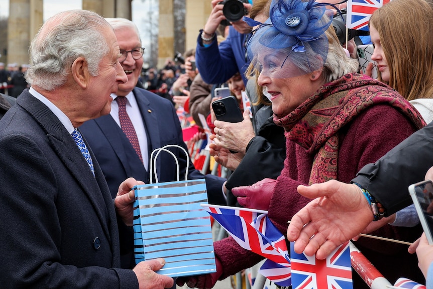 A woman in a blue fascinator speaks to Charles over a barricade 