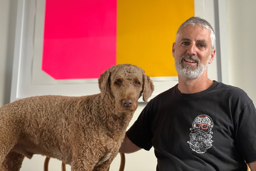 Man and dog sitting in front of artwork.