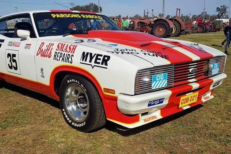 A racecar with stickers all over it parked on dry grass.