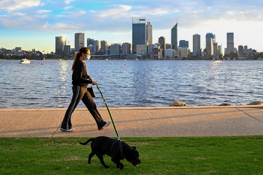A woman wearing a mask and a tracksuit walks along the South Perth foreshore.