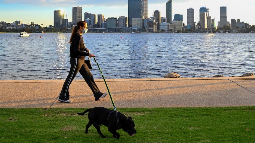 A woman wearing a mask and a tracksuit walks along the South Perth foreshore.