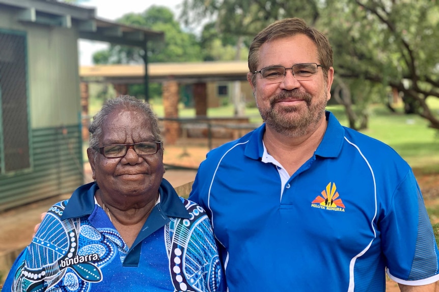 A man and woman, wearing blue shirts, stand side by side outside