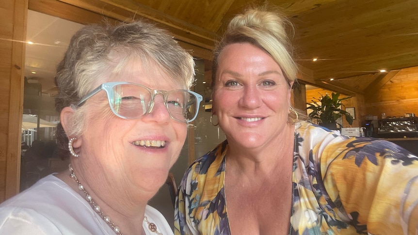 Two middle aged women look at the camera and smile as they pose for a selfie.