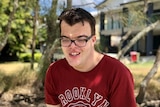 young man smiling, wearing blackglasses and maroon top on a sunny day