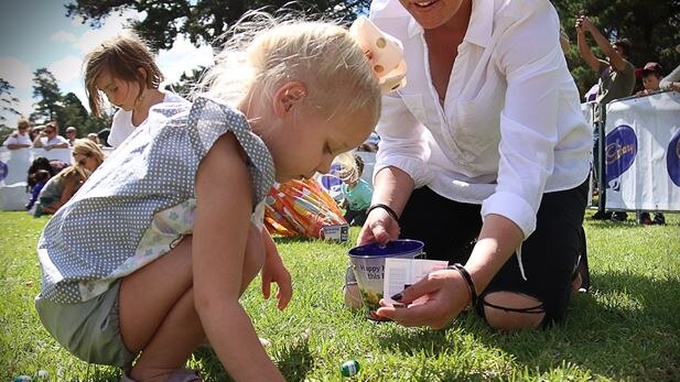 A child picks up an Easter egg off the grass during an Easter egg hunt.