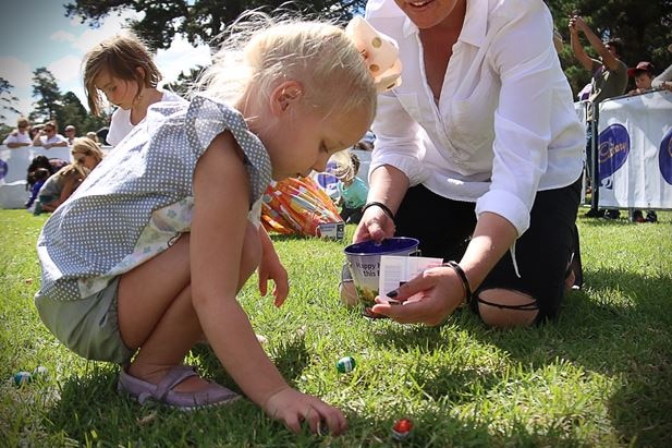 A child picks up an Easter egg off the grass during an Easter egg hunt.