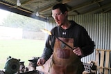 a blacksmith holds a steel rod in one hand and a chunk of beeswax in the other