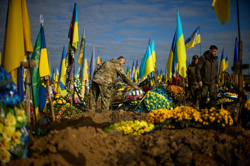一名乌克兰士兵在拥挤的墓地的坟墓上献花。