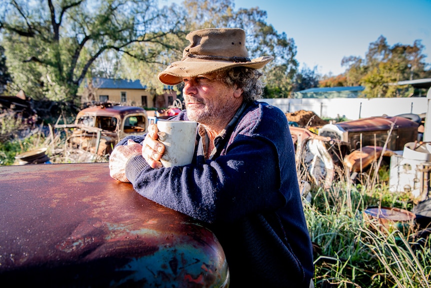 A man with a cup of coffee in a junkyard.