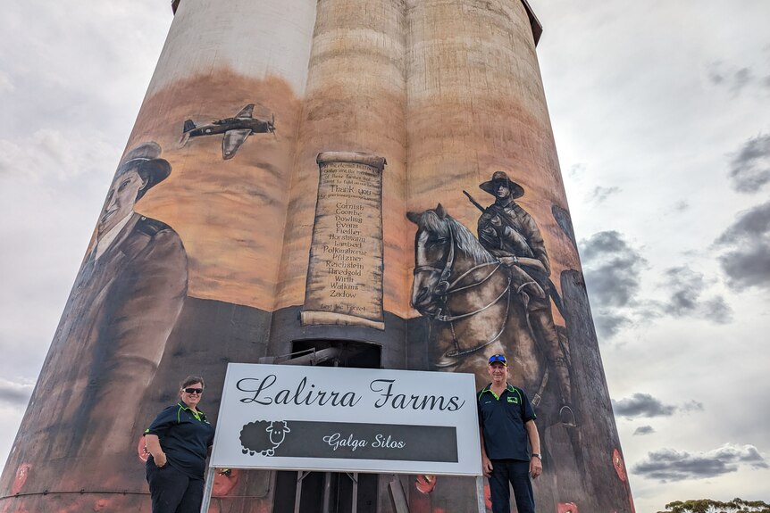 Beverly and Trevor Heidrich stand next to a Lalirra farms sign in front of the ANZAC remembrance silo art.