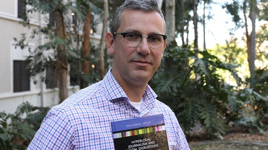 A man holds a book in his hands and stares at the camera.