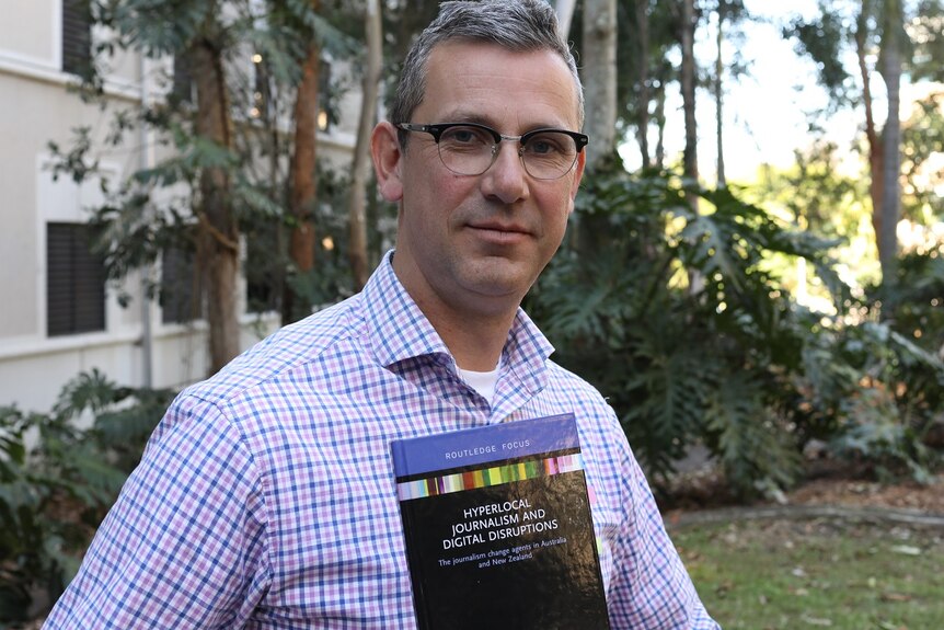 A man holds a book in his hands and stares at the camera.