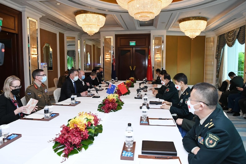 Australian officials sit in front of Chinese officials at long white tables decorated with country flags