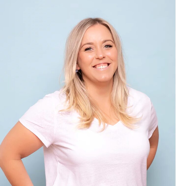 A headshot of a blonde lady wearing a white shirt smiling