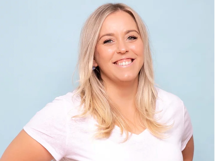 A headshot of a blonde lady wearing a white shirt smiling