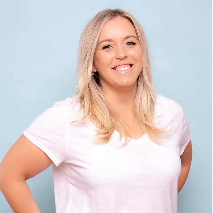 A headshot of a blonde lady wearing a white shirt smiling