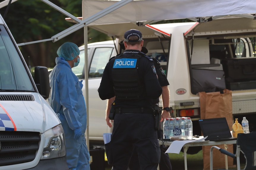 A uniformed police officers stands next to a forensics investigator dressed in a blue suit.