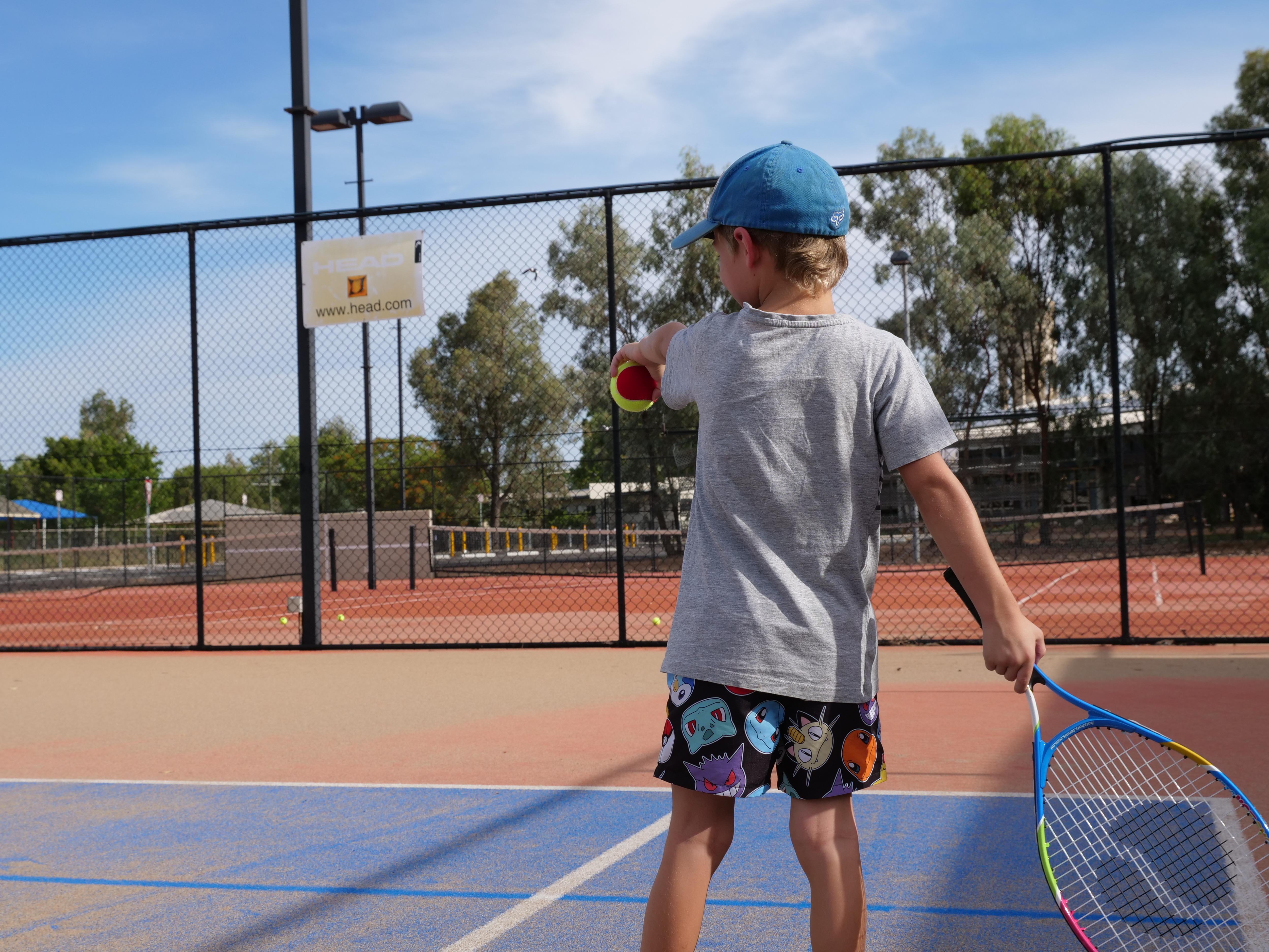 A young boy on a tennis court on a sunny day.