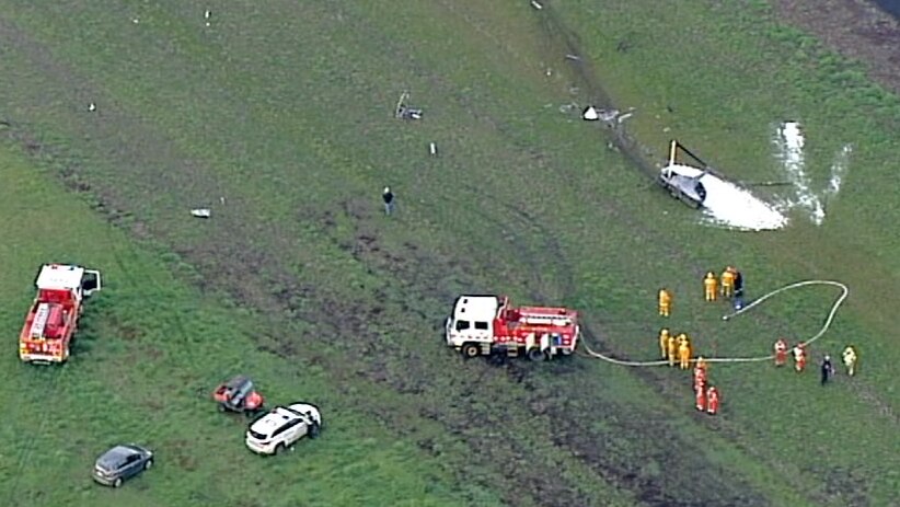 A damaged helicopter in a field, surrounded by emergency service workers.