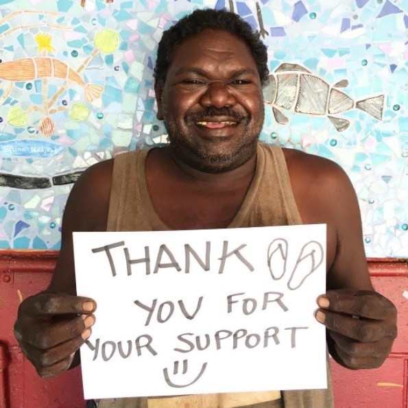 Gabriel Maralngurra holds a sign thanking supporters after a crowdfunding campaign.