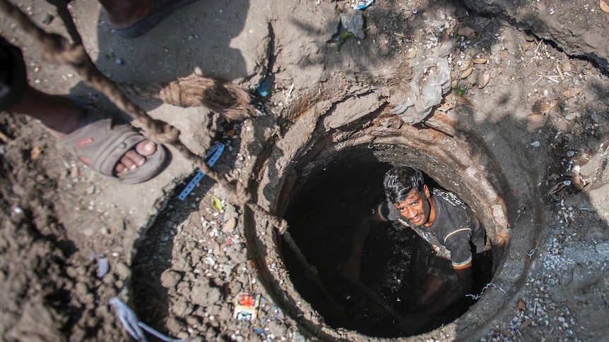 Man looks up from the man hole which he is sitting in.