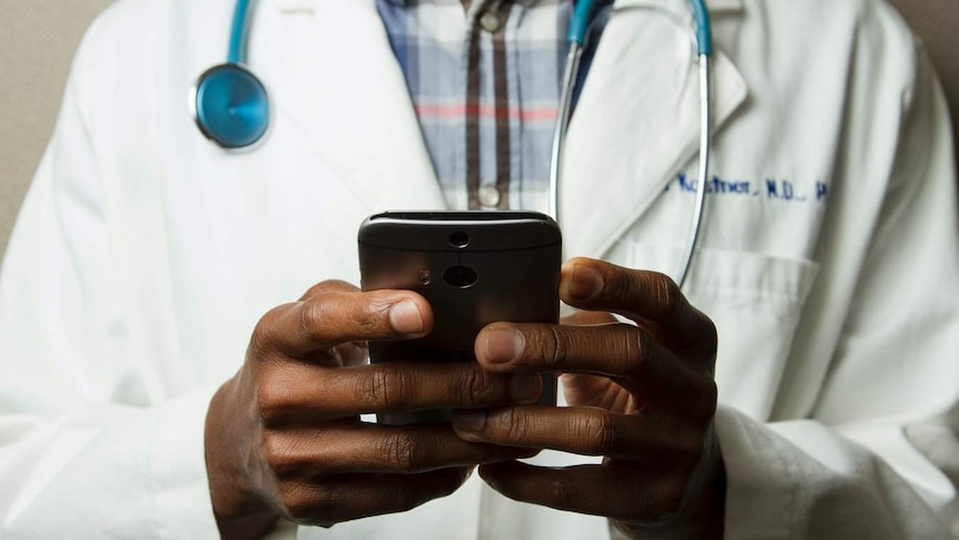 The torso of a person wearing a medical coat and stethoscope and holding a smartphone.