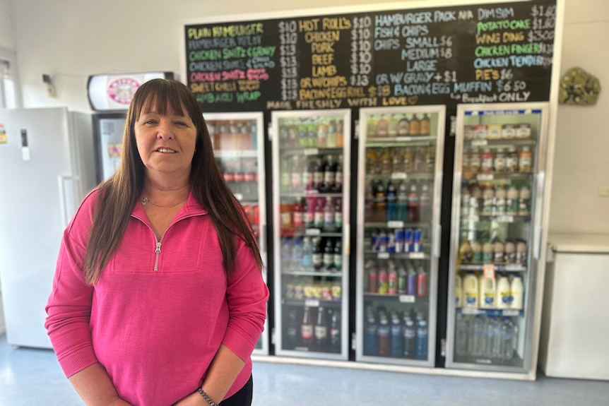 woman in bright pink jumper standing in front of large drinks fridge and takeaway menu with most items ten dollars