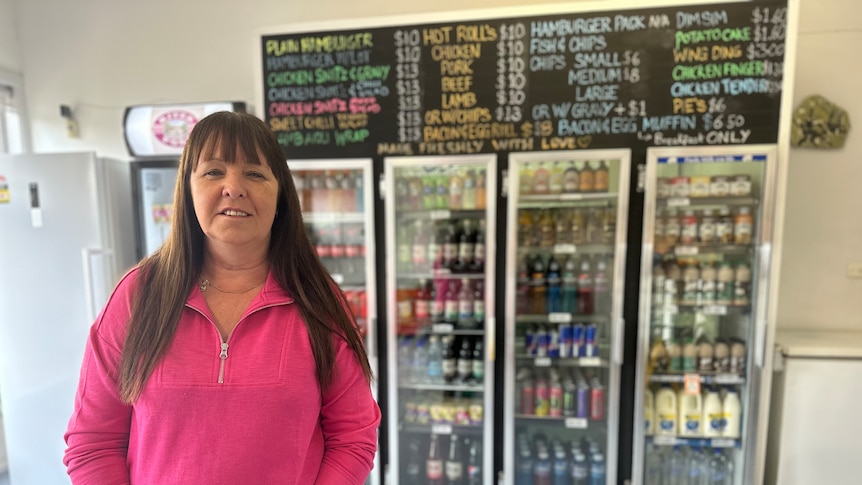 woman in bright pink jumper standing in front of large drinks fridge and takeaway menu with most items ten dollars