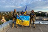 Ukrainian soldiers hold a flag at a rooftop in Kupiansk.