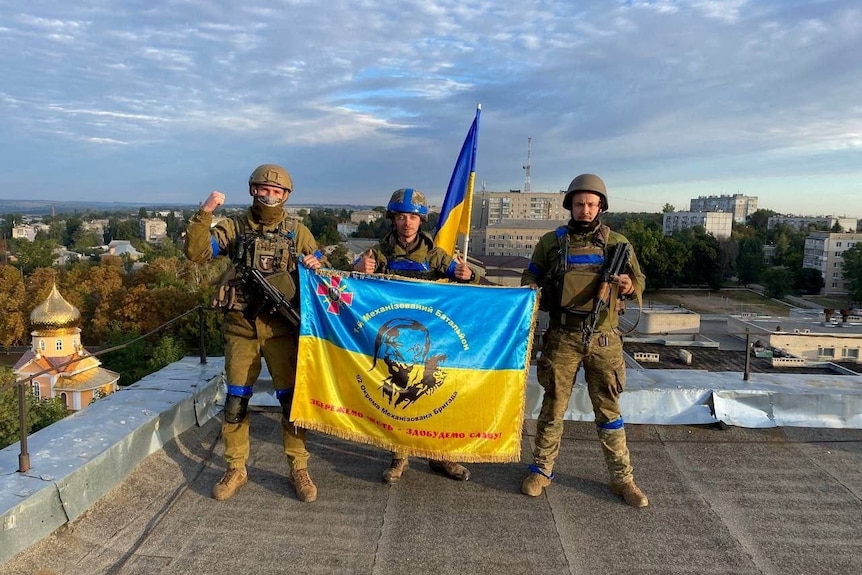 Ukrainian soldiers hold a flag at a rooftop in Kupiansk.
