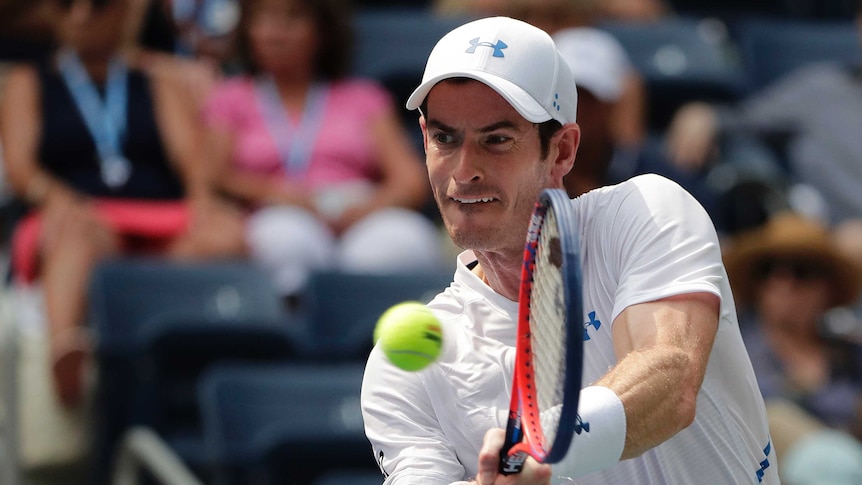 A tennis player hits a return, with the ball coming off the racquet.