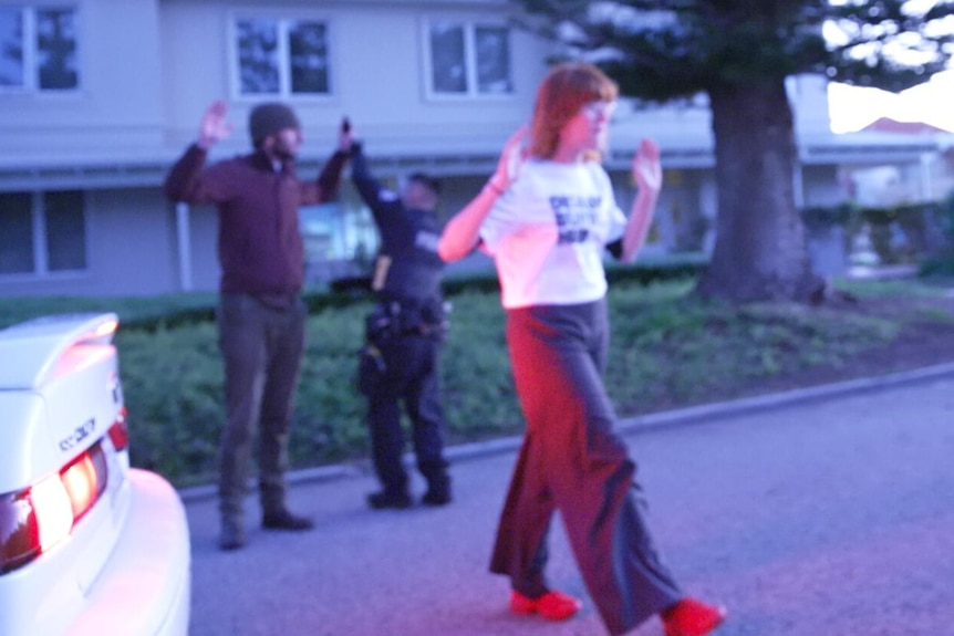 A woman in a 'DISRUPT BURRUP HUB' T-shirt stands in the street with her arms raised