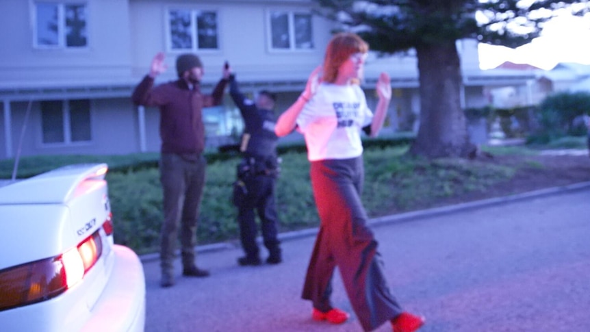 A woman in a 'DISRUPT BURRUP HUB' T-shirt stands in the street with her arms raised