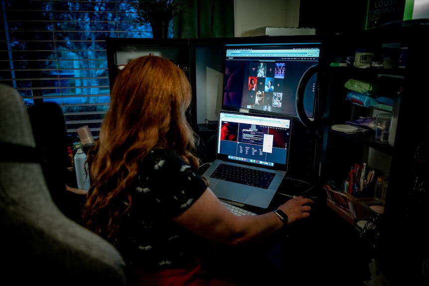 Back of woman as she looks at computer screens on desk.