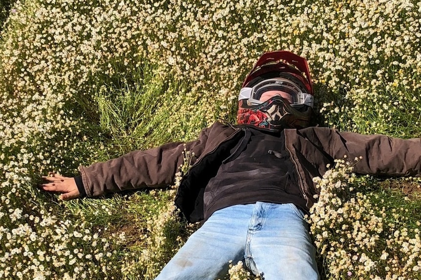 A child laying on a bed of wildflowers with a motorbike helmet on