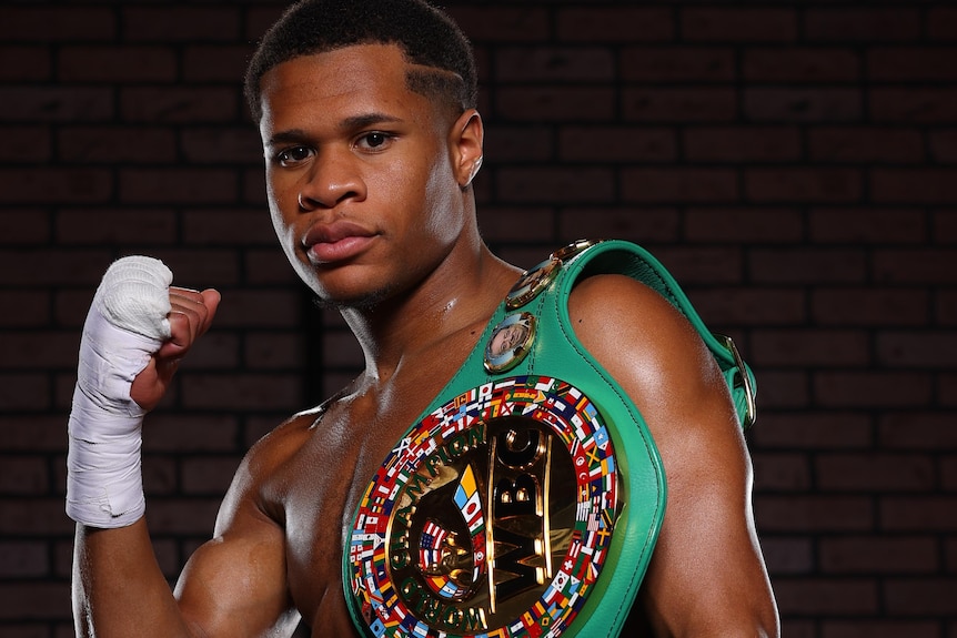 Devin Haney holds up a strapped right fist with the WBC belt draped over his left shoulder