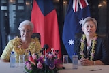 Two women sit at a table in front of the flags of Samoa and Australia