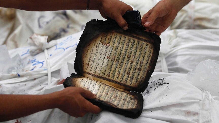 Two people hold a partially burnt copy of the Koran next to the bodies of Mohammed Morsi supporters.