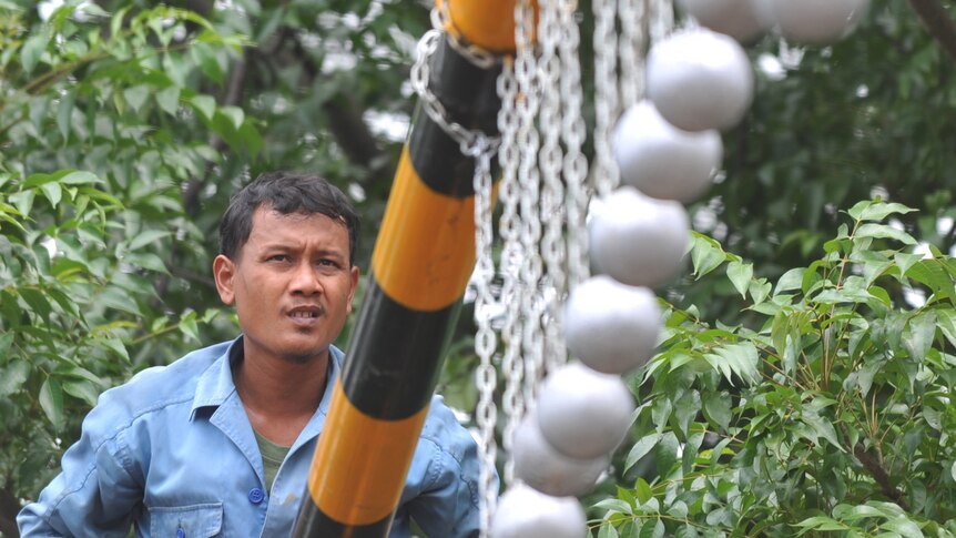 A worker installs an iron support with hanging concrete balls to deter train surfers.