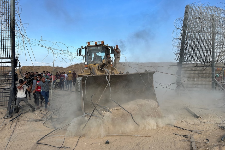 A bulldozer crashes through a metal chain link fence 