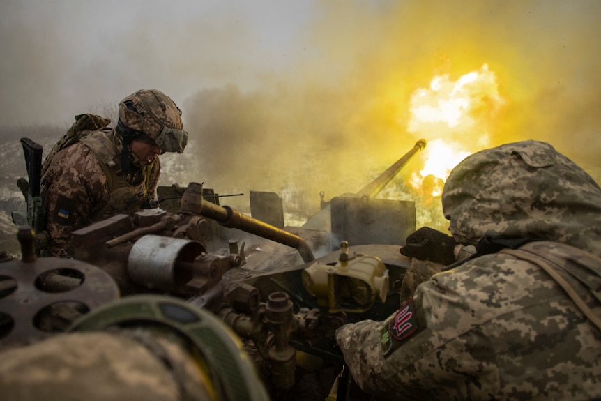 Two servicemen fire an anti-aircraft gun, with fire seen coming out.