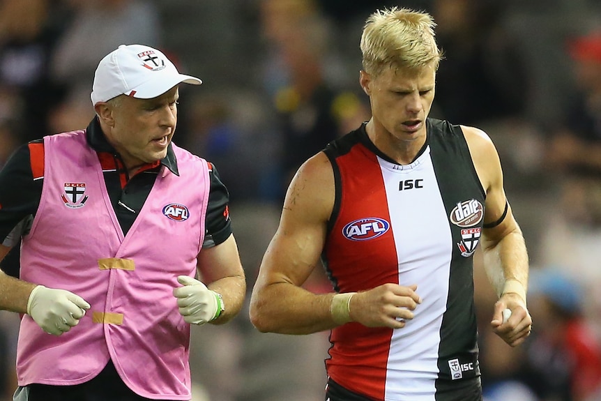 Nick Riewoldt jogs off the field flanked by two trainers during an AFL game.