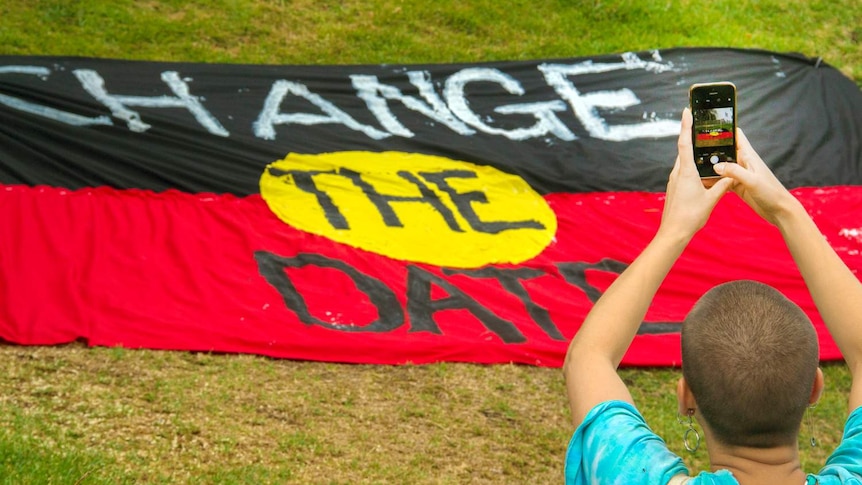 An Aboriginal flag with the words 'change the date'