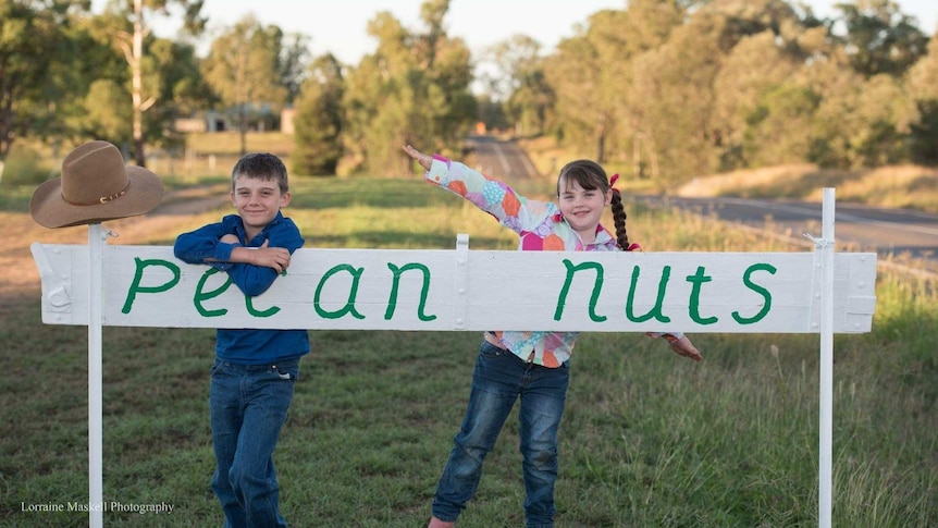 A boy and a girl stand behind a white sign reading pecan nuts