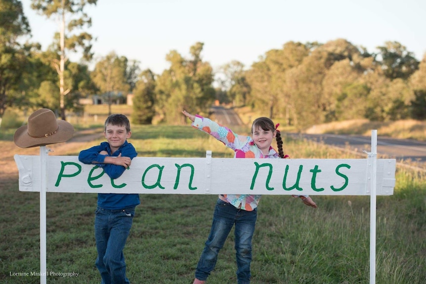 A boy and a girl stand behind a white sign reading pecan nuts