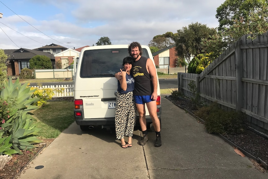 Tracy and Dan smiles and hug posing in front of a white van in a suburban driveway