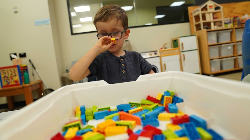 Young boy holds an orange piece of Lego up to his face.