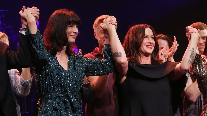 A group of people, including Diablo Cody and Alanis Morissette, holding hands and taking a bow on stage.